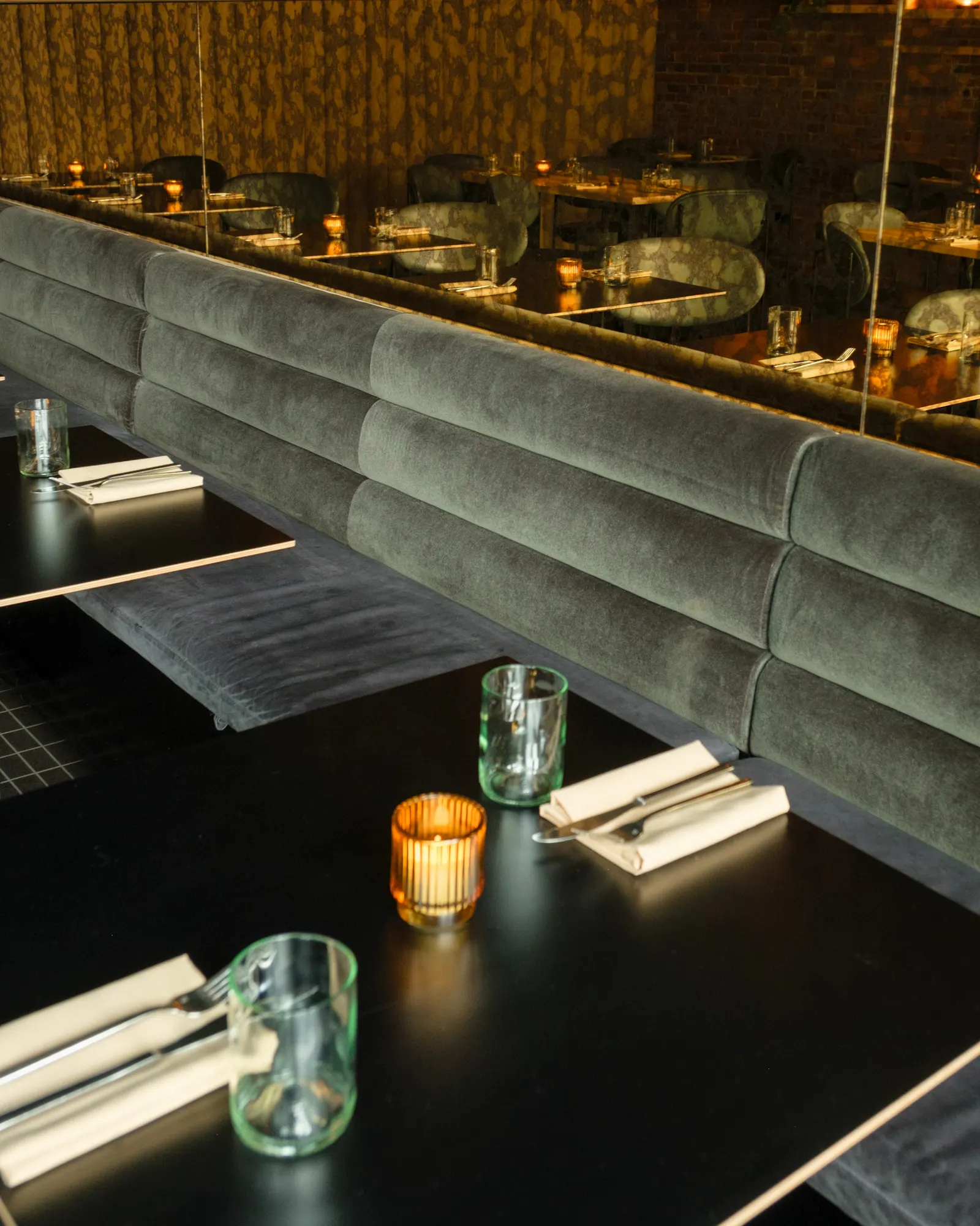 Green velvet along the wall, with dark tables in front of it.
