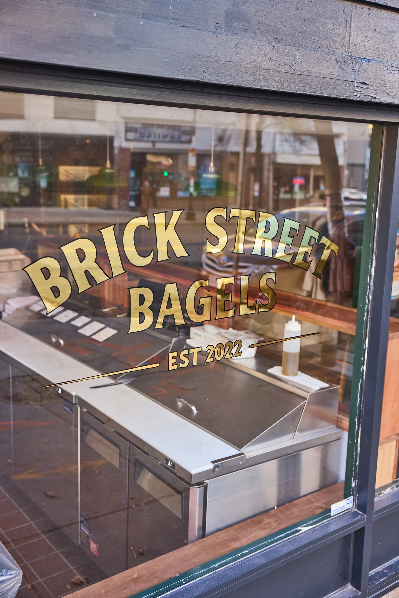 The gold-leaf sign on the shop window, seen from the street, with the counter inside behind the glass.