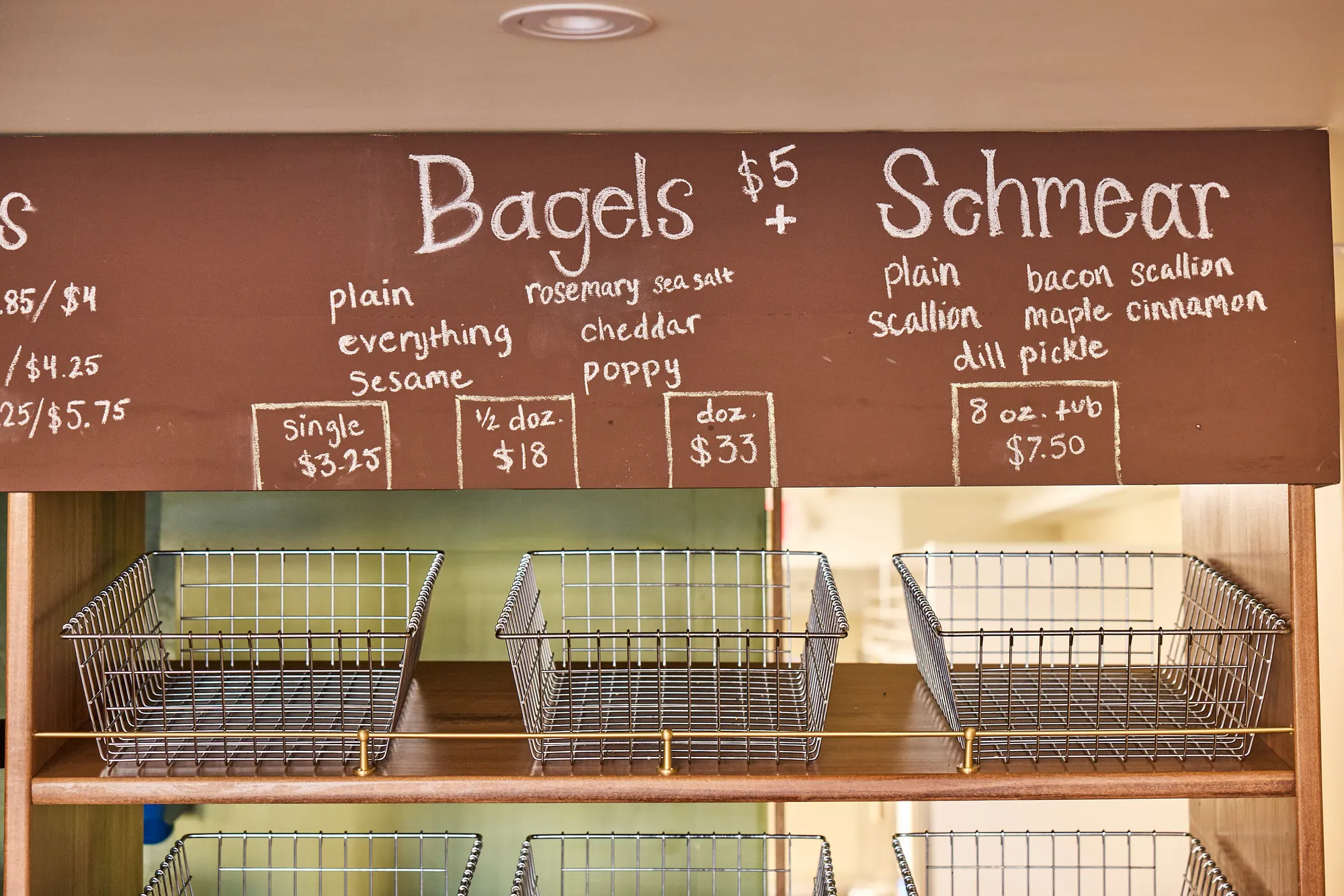 The hand-lettered bagel and schmear board above a row of empty wire baskets.