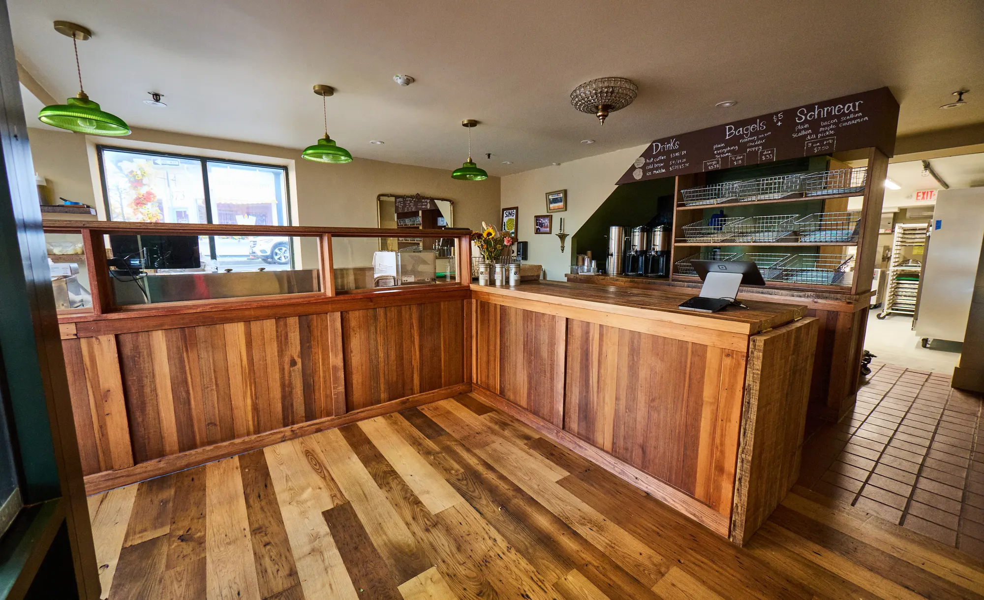 An L-shaped counter in reclaimed timber on a floor of mixed boards, under green glass pendants.