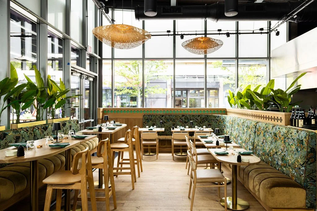 Leaf-print banquettes and timber chairs, under rattan pendants against the glazing.