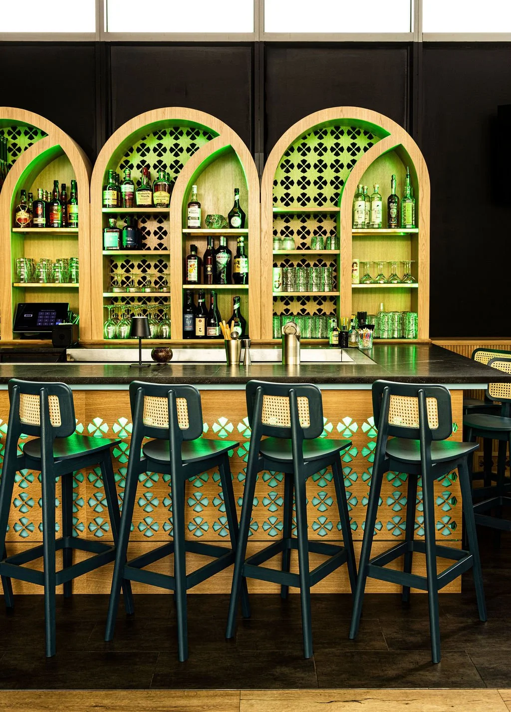 Green stools against a patterned bar front, under three of the arches.