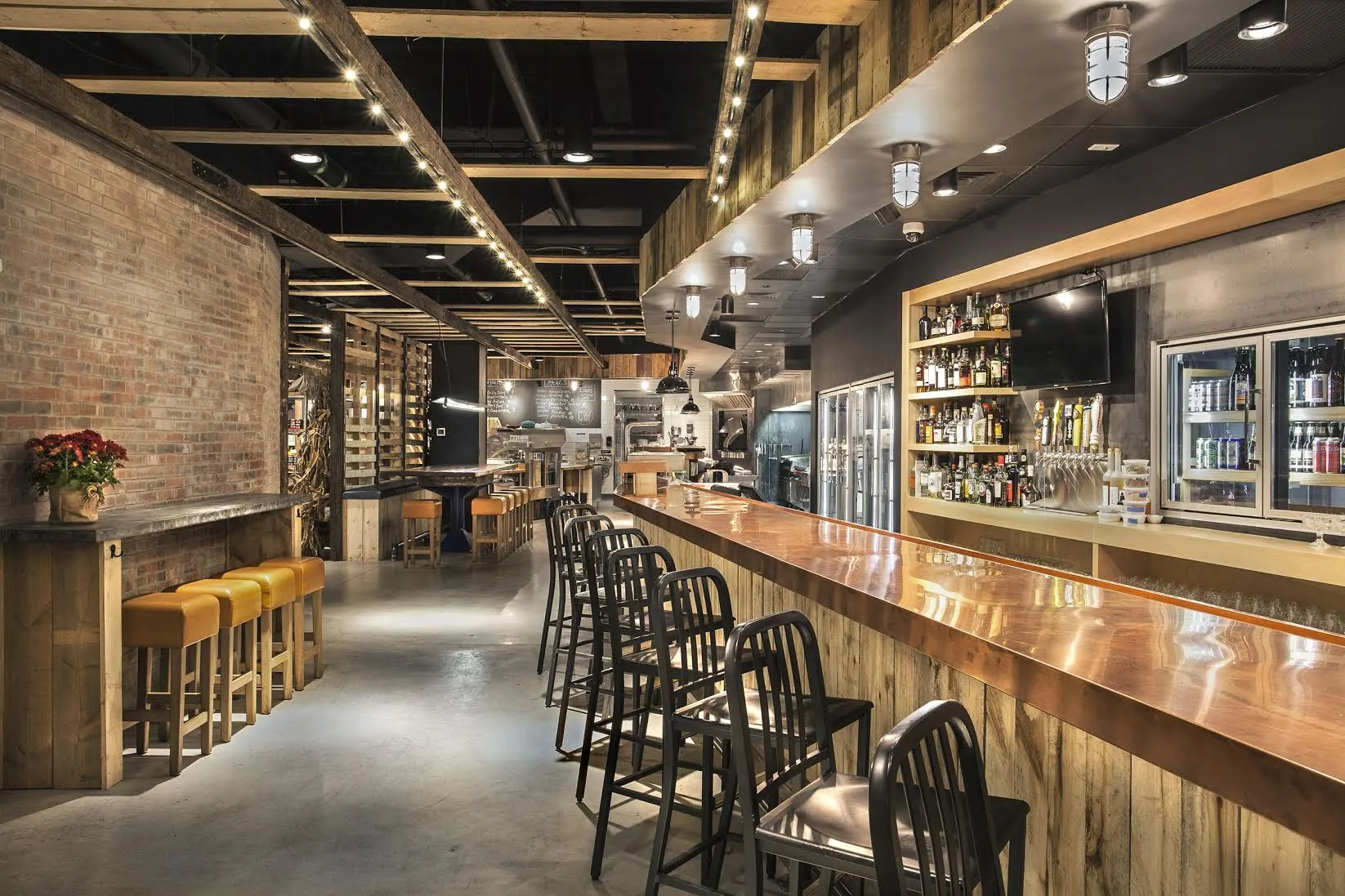 A long copper-topped bar with black stools, beside brick and timber walls.