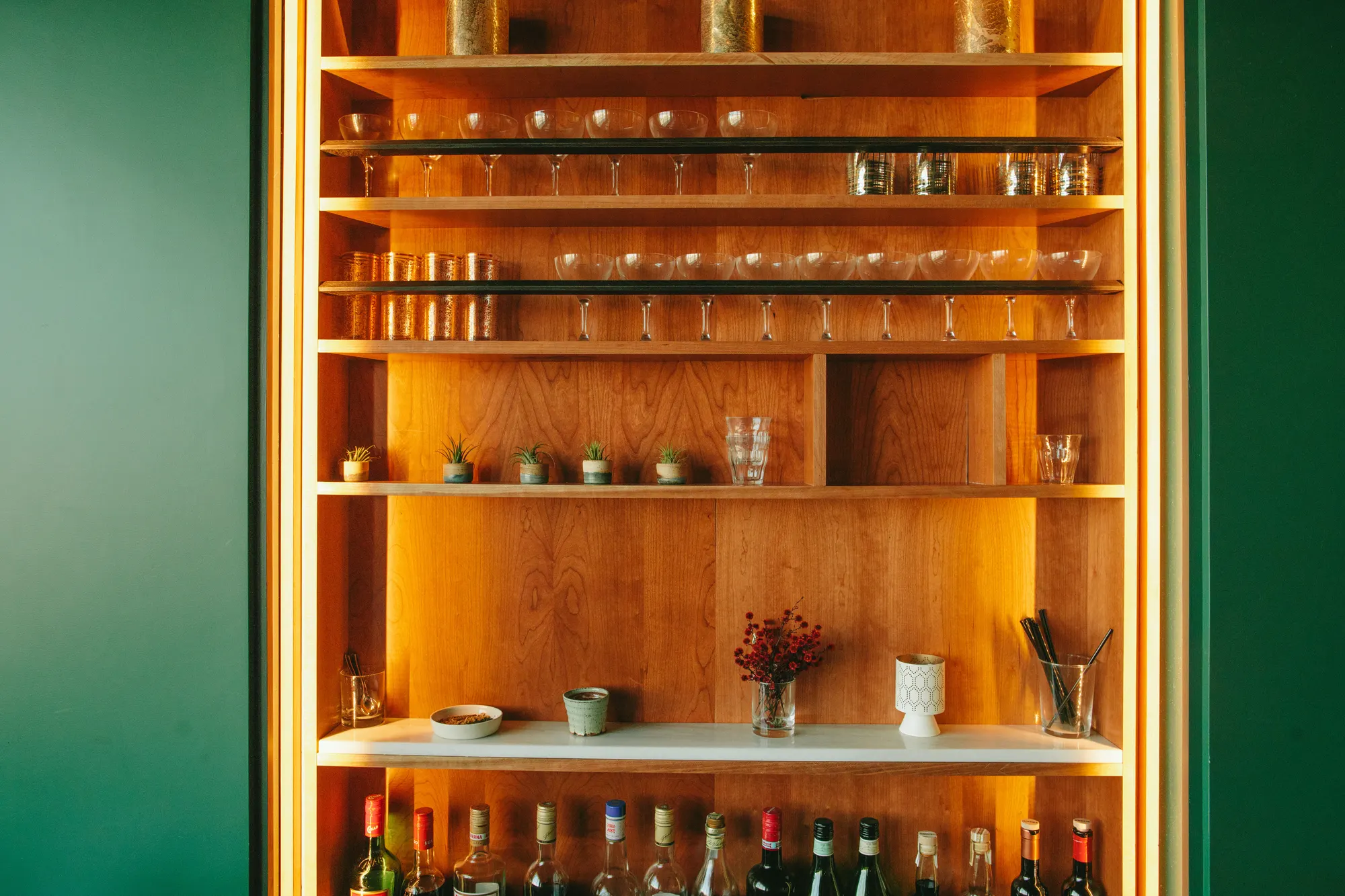 Glassware, preserves and bottles on open shelves, lit from inside the recess.