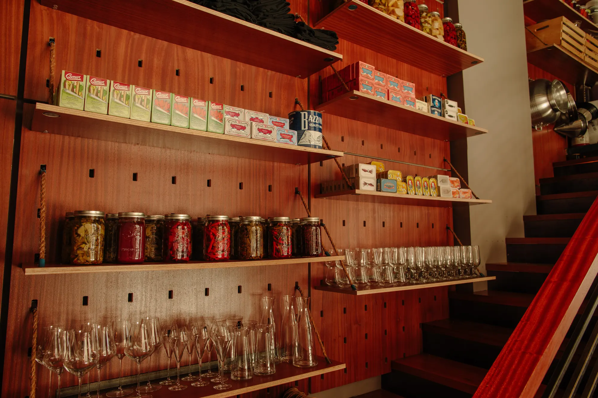 Tinned fish and preserves above, glassware below, on a pegged timber wall that runs the length of the room.