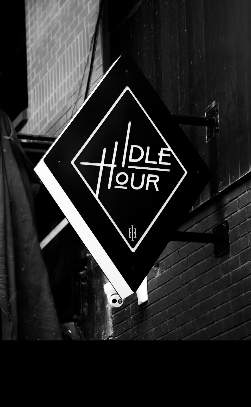 A diamond sign reading Idle Hour, hanging from a brick wall.