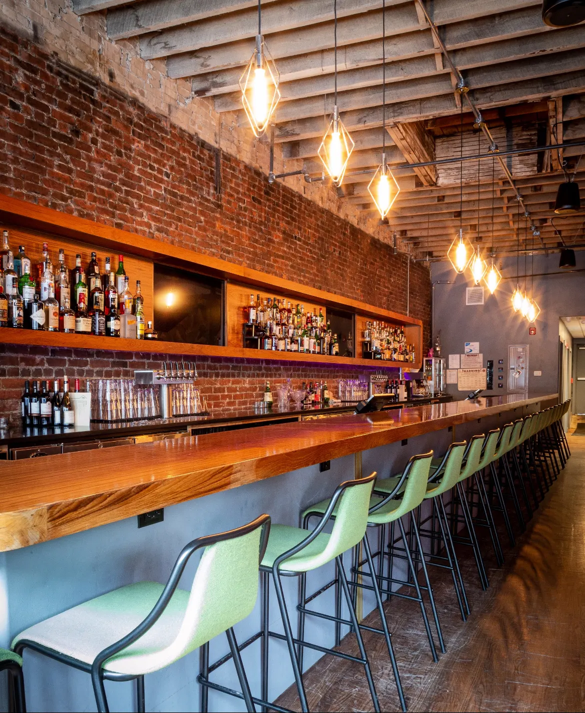 The bar at Idle Hour, pale green stools along a long timber bar under diamond pendants