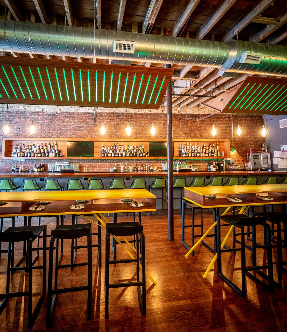 Yellow-framed high tables and black stools in front of the back bar.