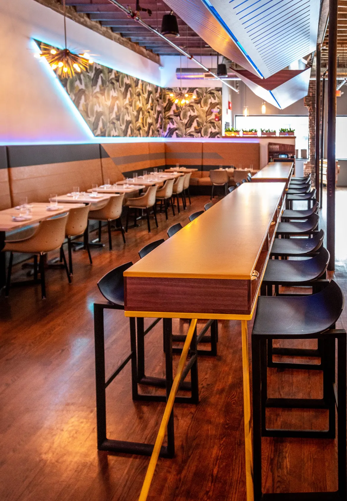 A long banquette and a high table under the palm-print mural.
