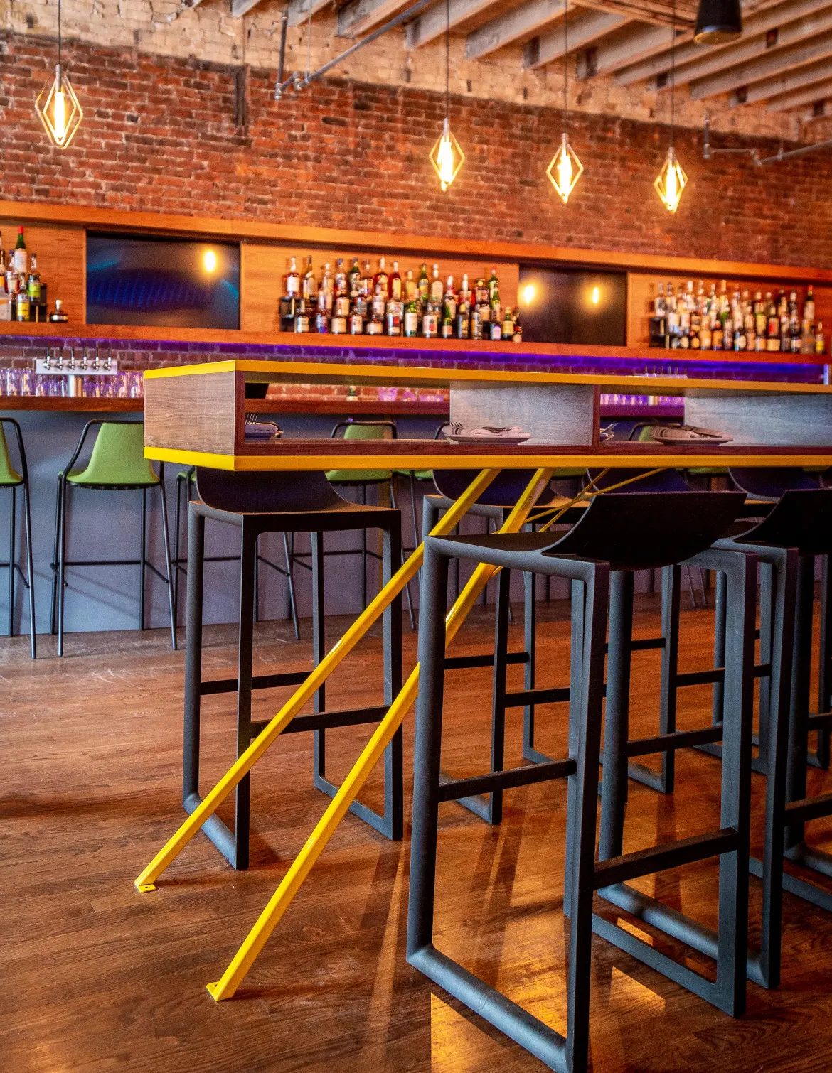 Yellow high tables and stools in front of the brick back bar.