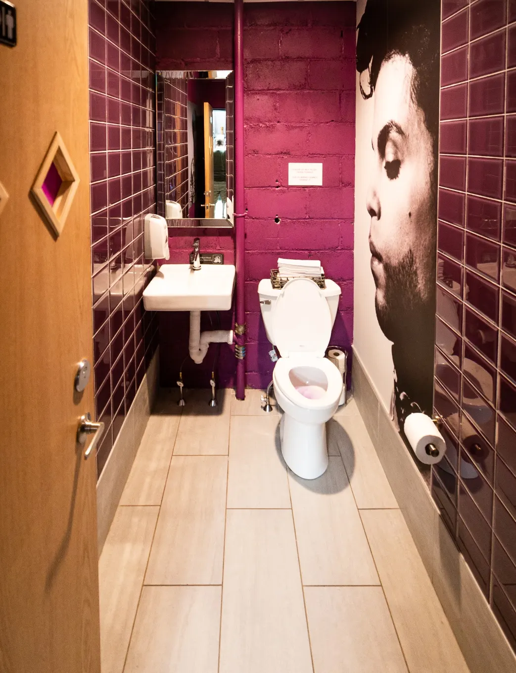 A restroom in purple tile, with a large portrait on the wall.