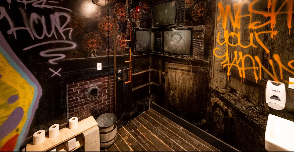 A restroom covered in graffiti, with old televisions on the wall.