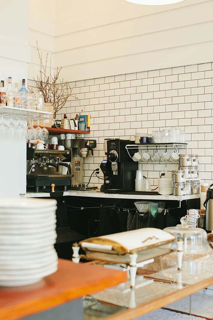 Stacked plates and an espresso machine on the counter, under open shelves.