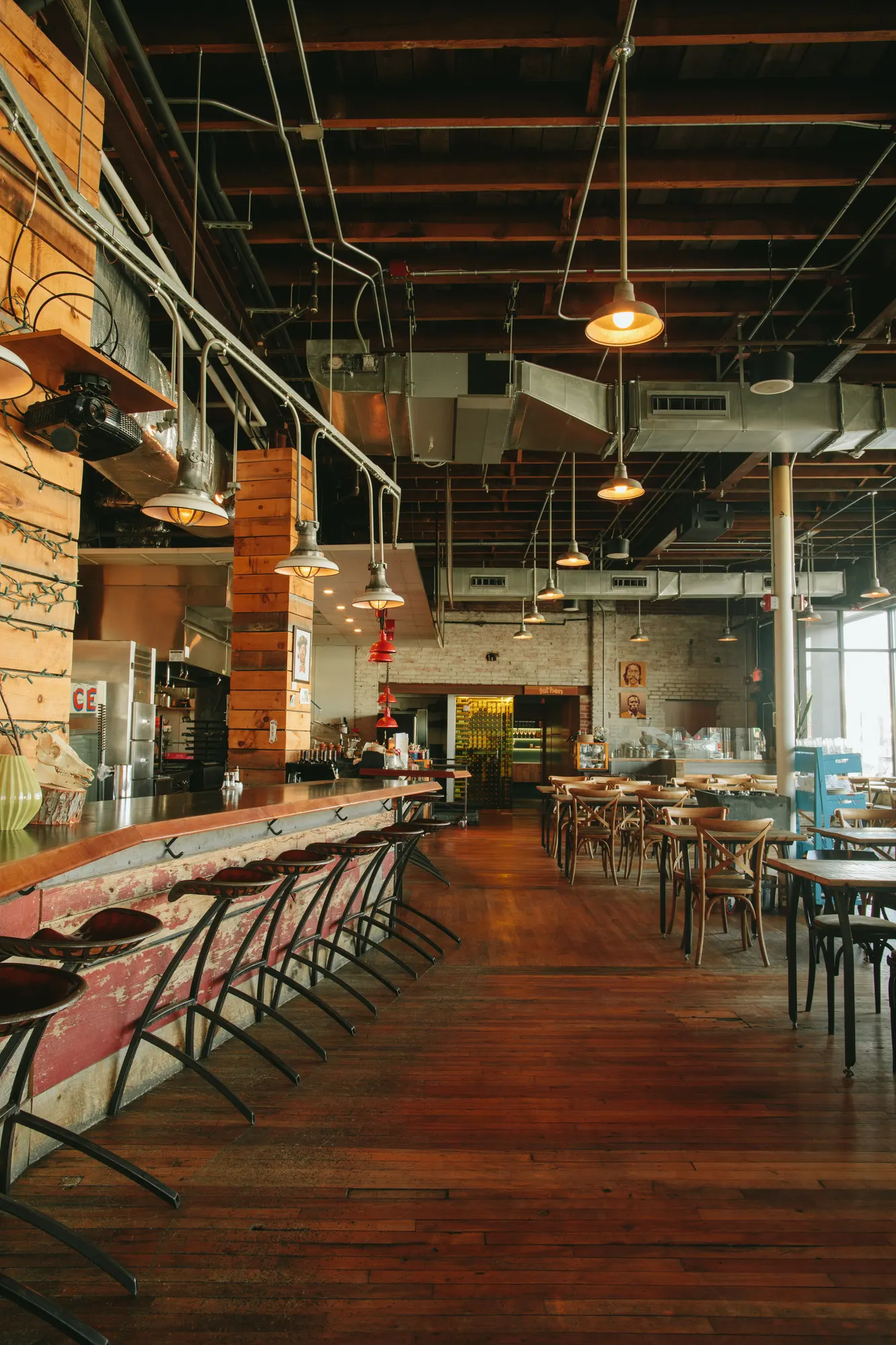 Stools along a red-painted bar front, running the length of the room under pendants hung from the open ceiling.
