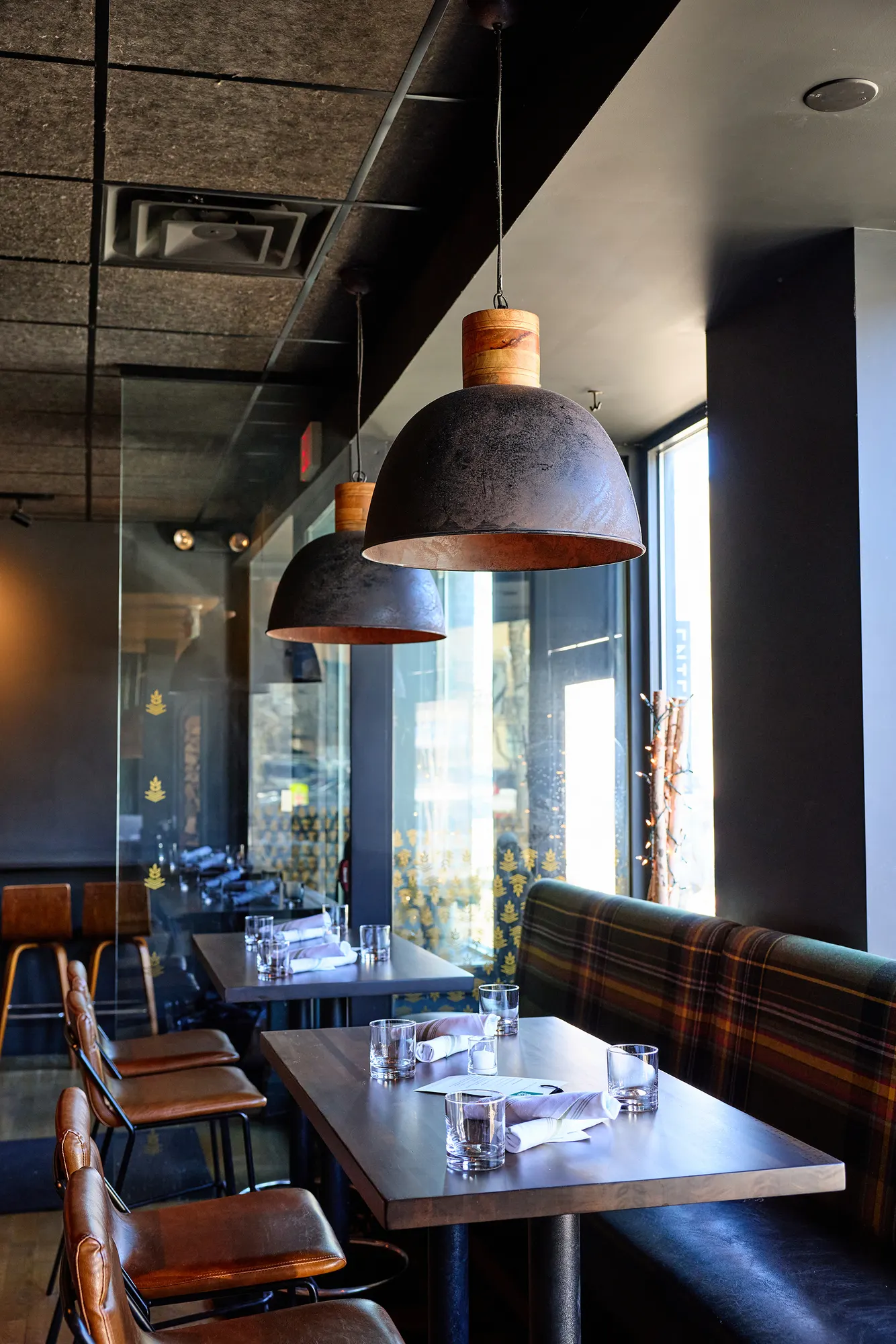Tables and leather chairs along a plaid banquette under dark dome pendants.