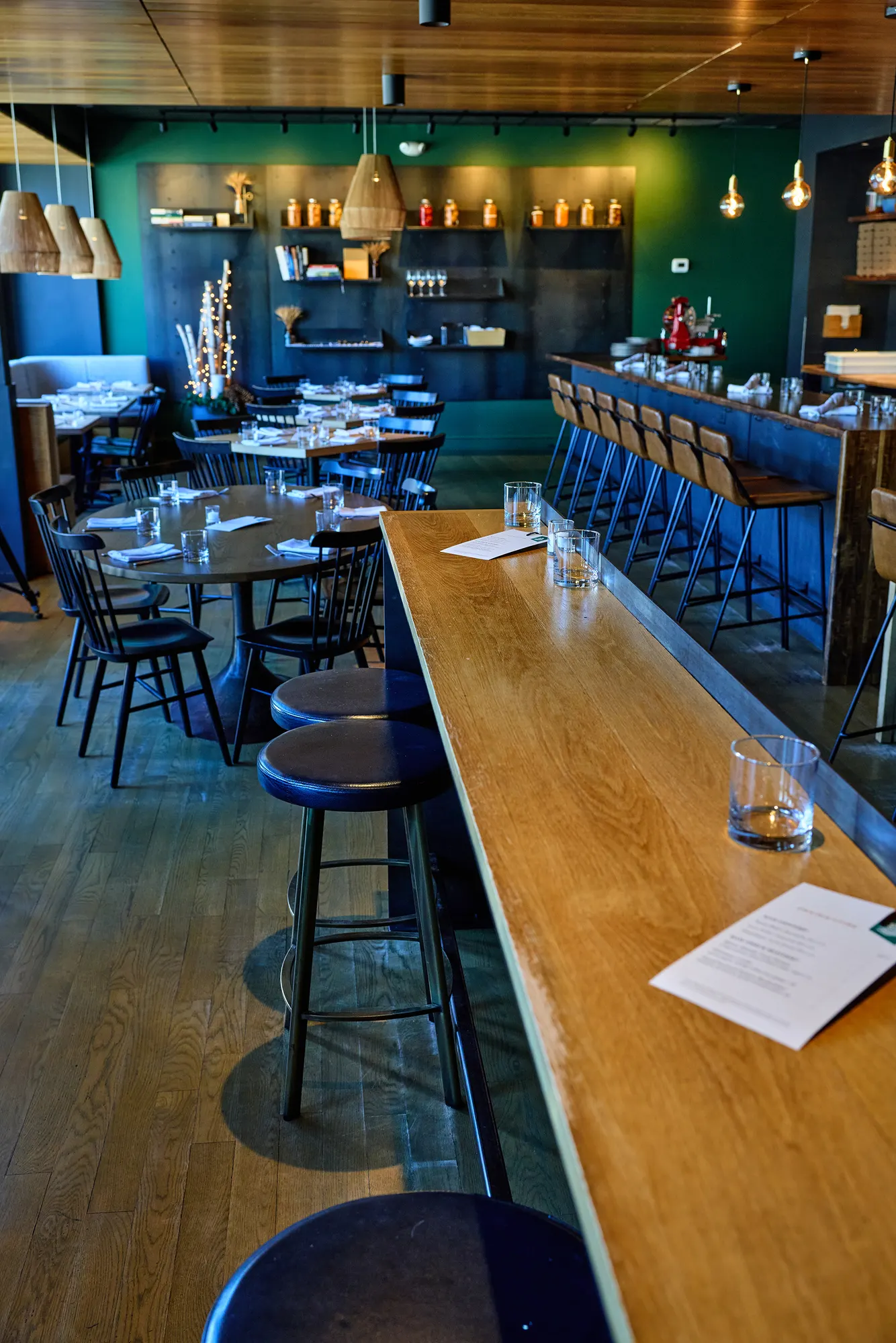 A long timber high table and stools, with the dining room and bar beyond.