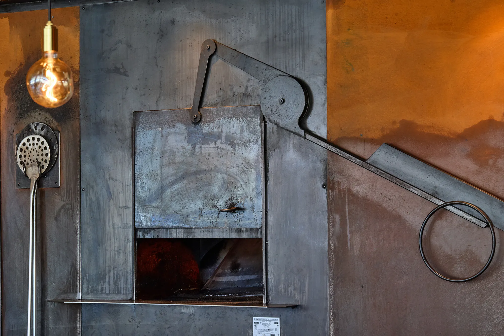 The oven's steel door and counterweighted arm, with a globe bulb beside it.