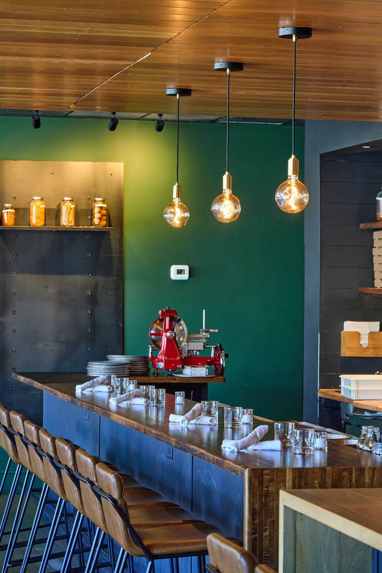 A red meat slicer on the counter below three globe pendants and the green wall.