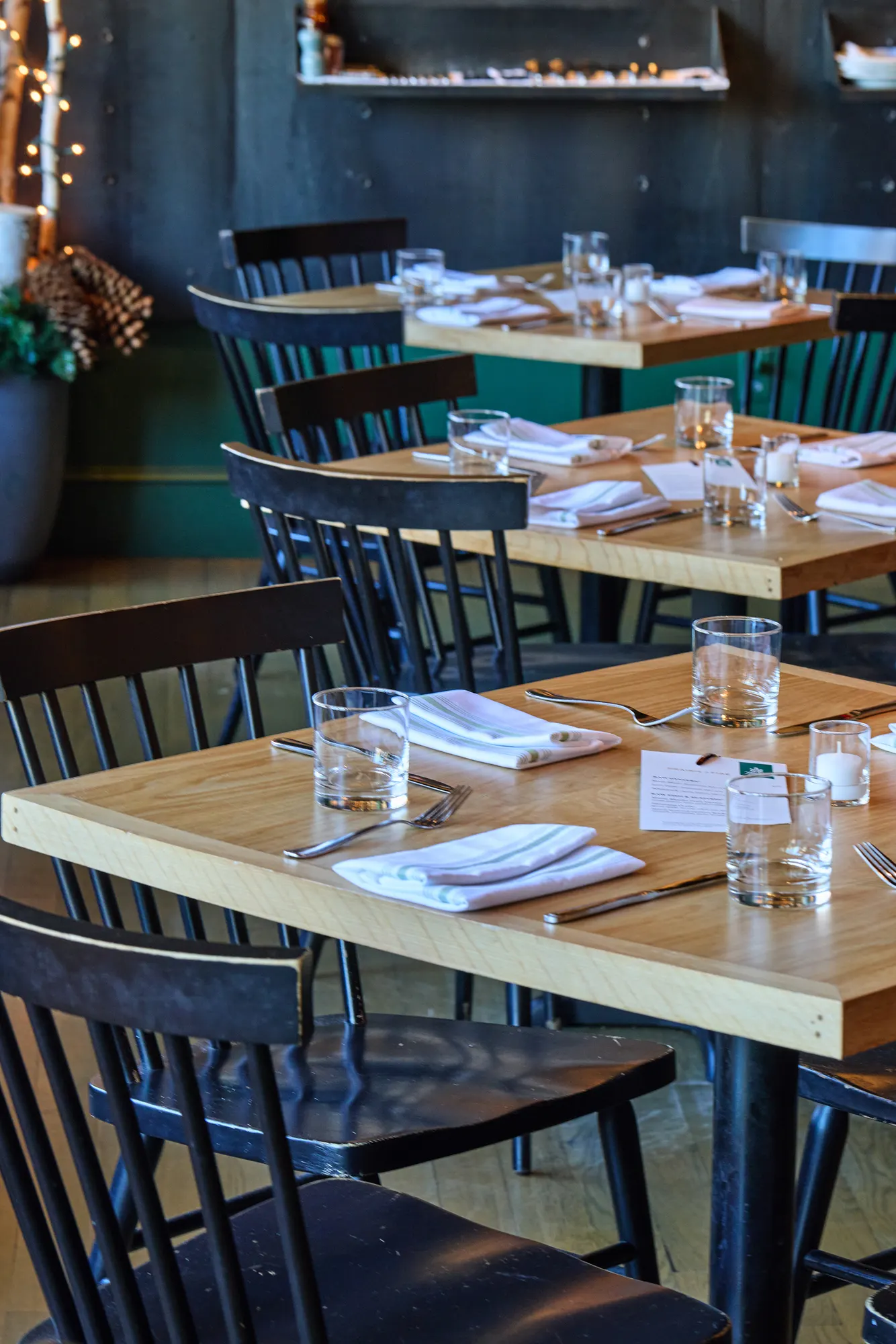 A row of tables set for dinner, with black spindle chairs.