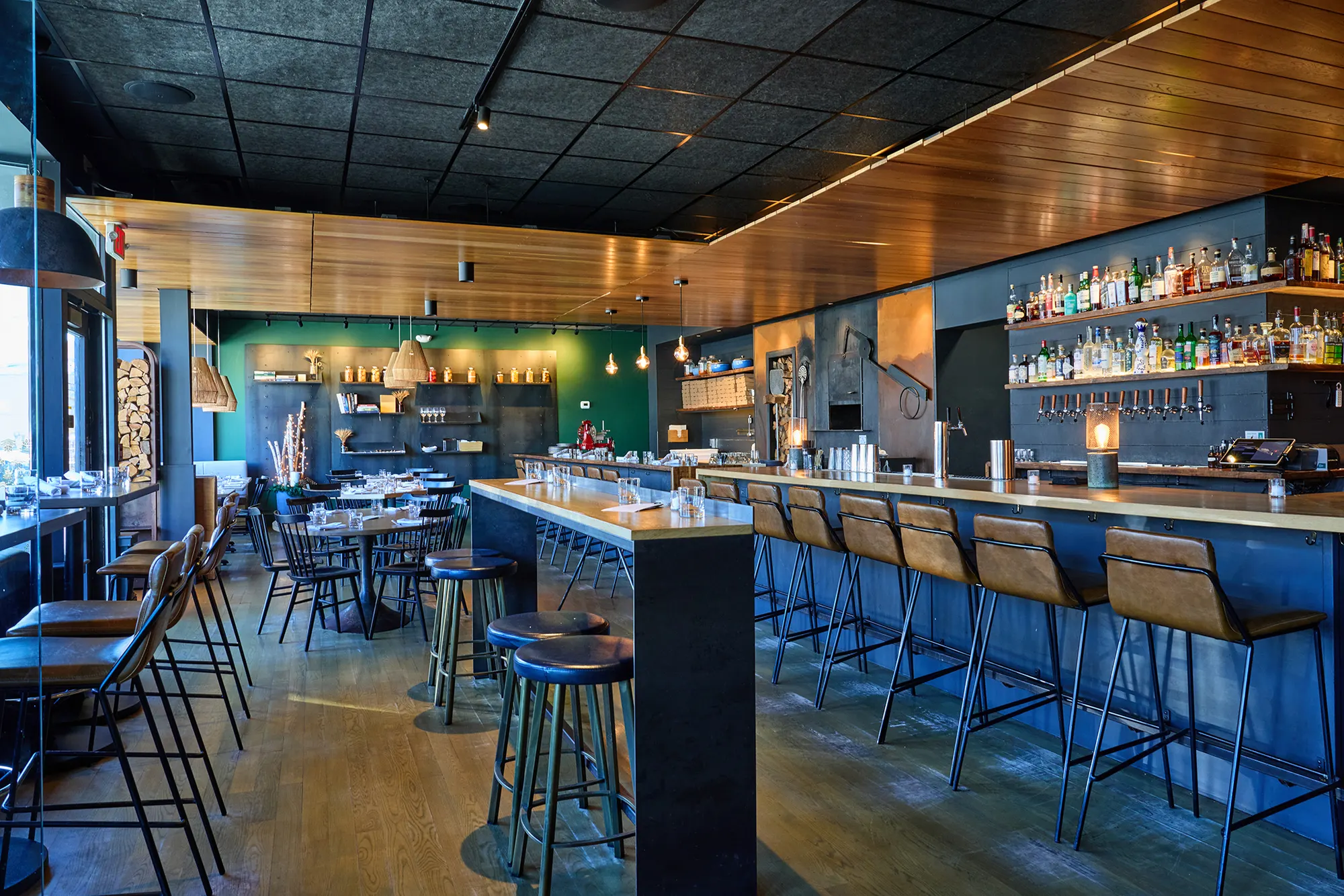 The long bar with its blue front and leather stools beside the dining room, under a timber ceiling.