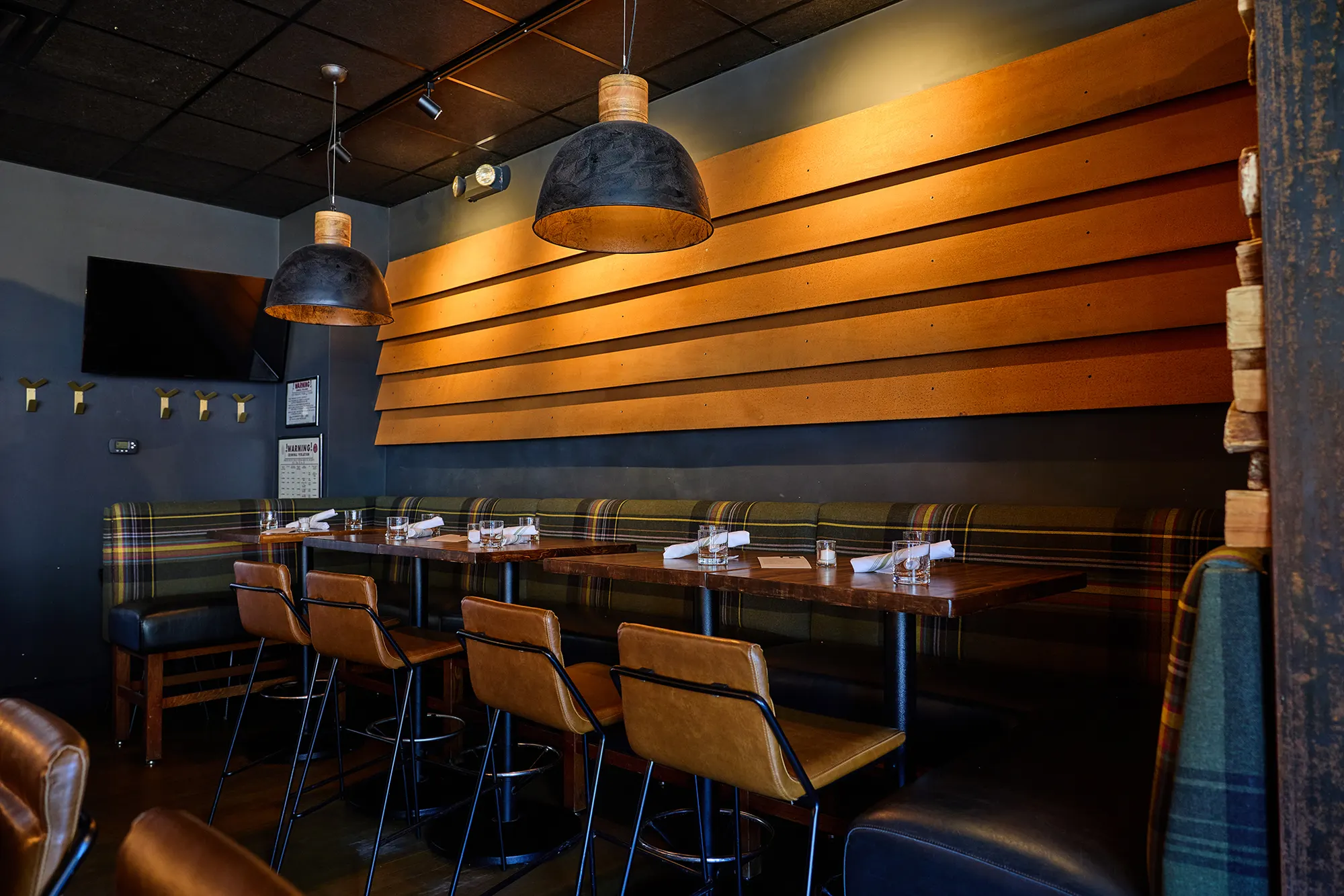 Tables along a plaid banquette under a wall of broad, warm timber boards.