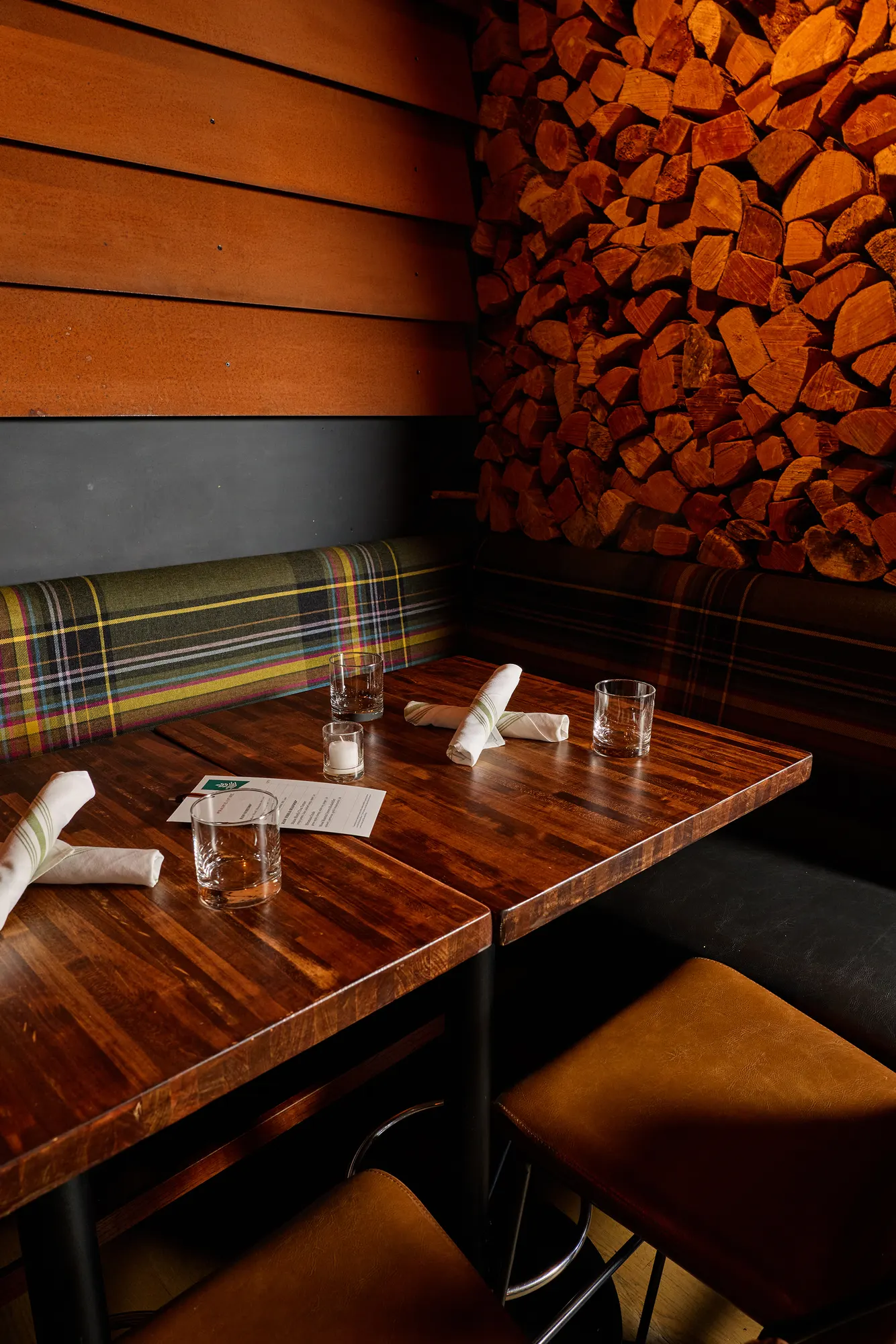 A walnut table on the plaid banquette, below the timber boards and firewood.