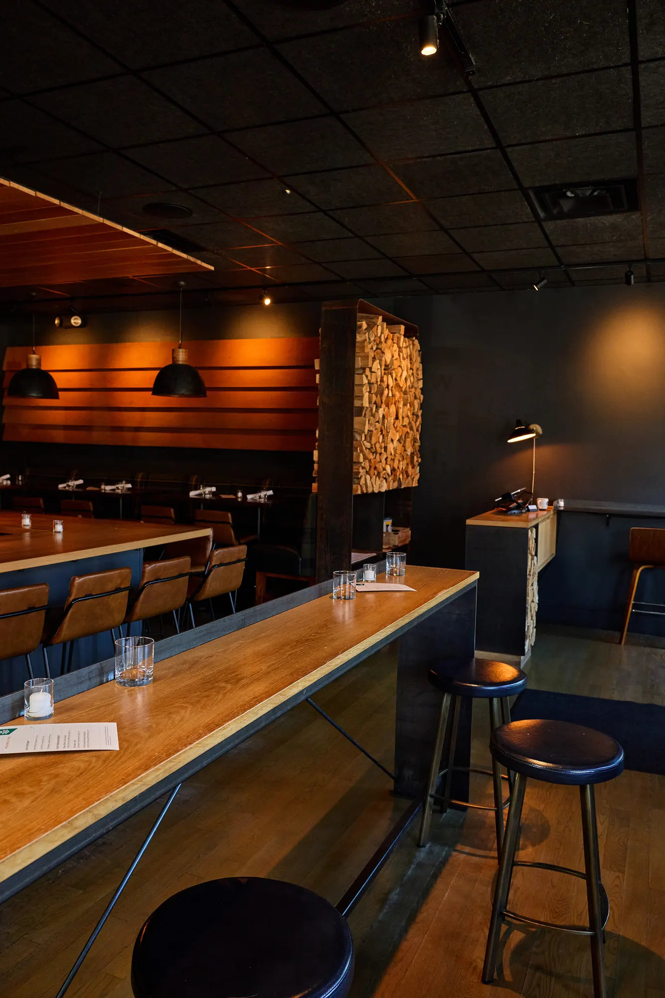 A long high table under a dark ceiling, with the timber wall glowing beyond.
