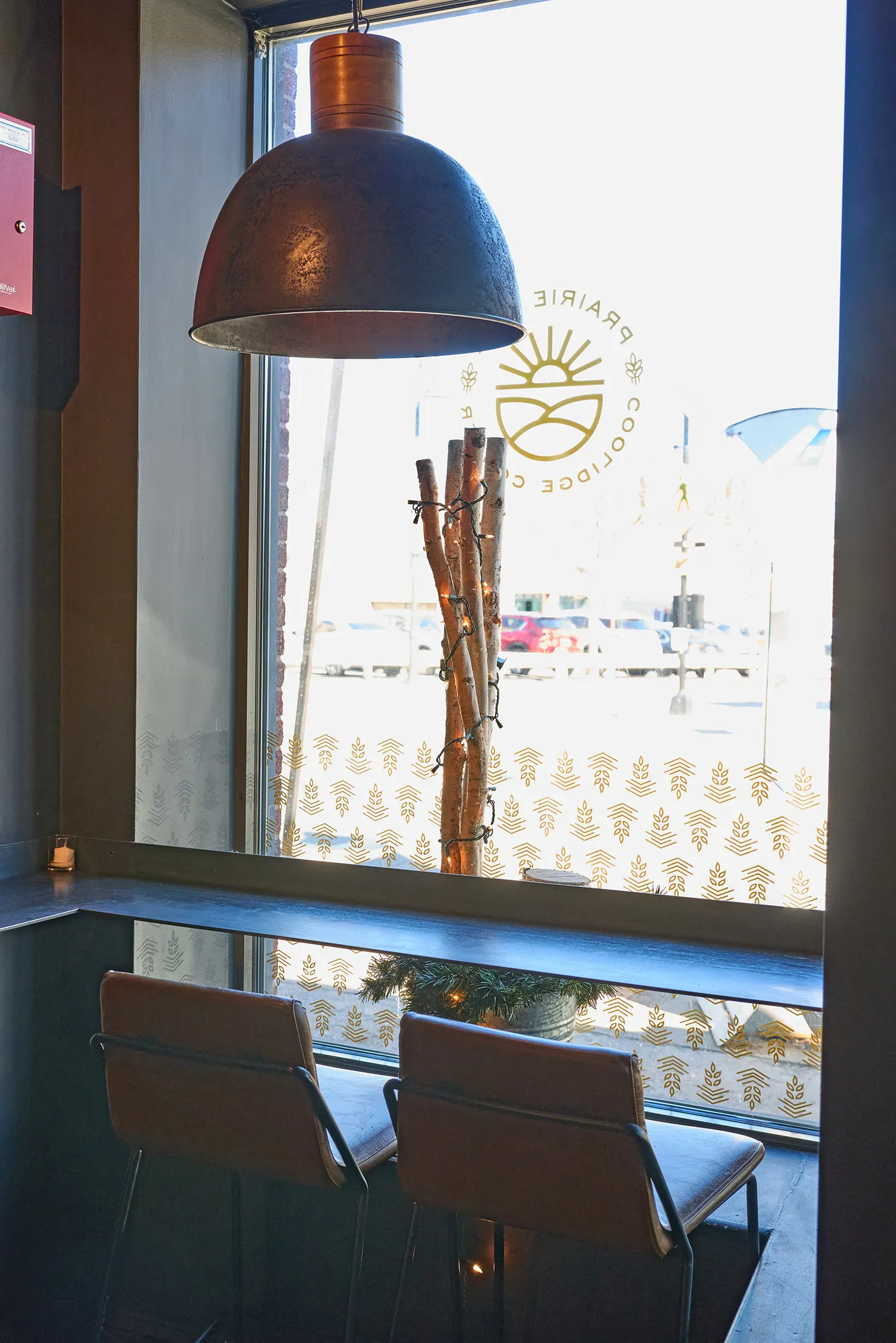 Leather stools at the window counter, with a dark pendant and the logo on the glass.