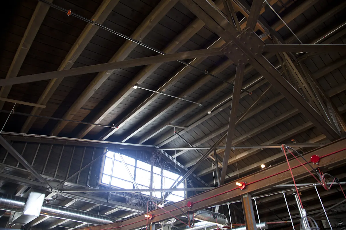 Steel trusses under the roof deck, lit by a window in the gable.