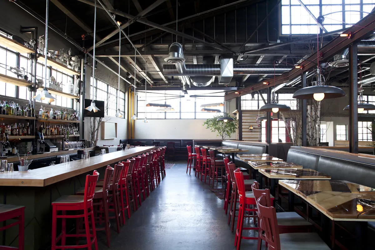 The bar at Steel & Rye, red stools the length of the room under the open steel roof