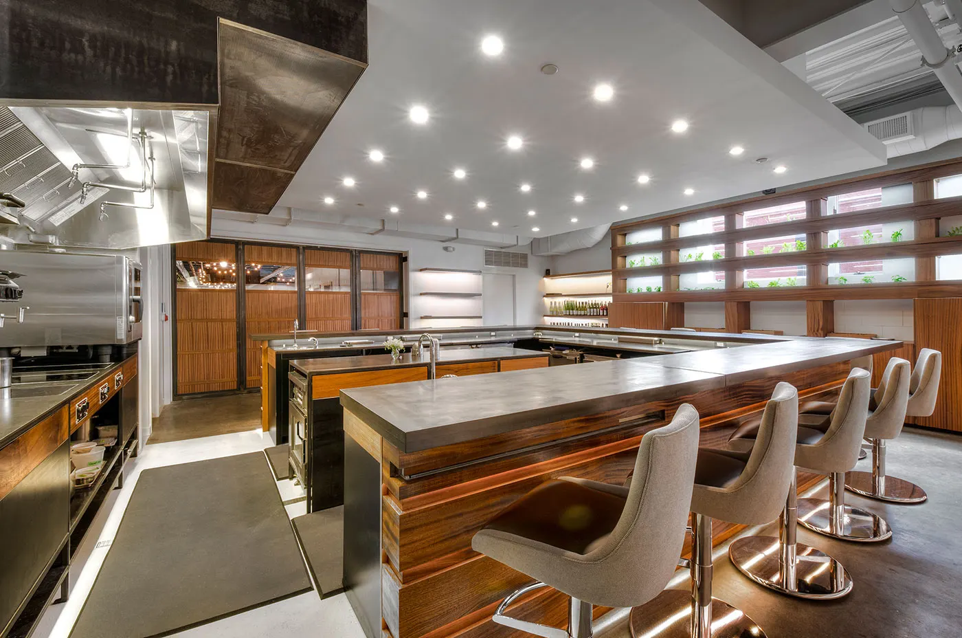 A concrete-topped counter wrapping the kitchen, with stools on the outside and herbs growing in the window behind.
