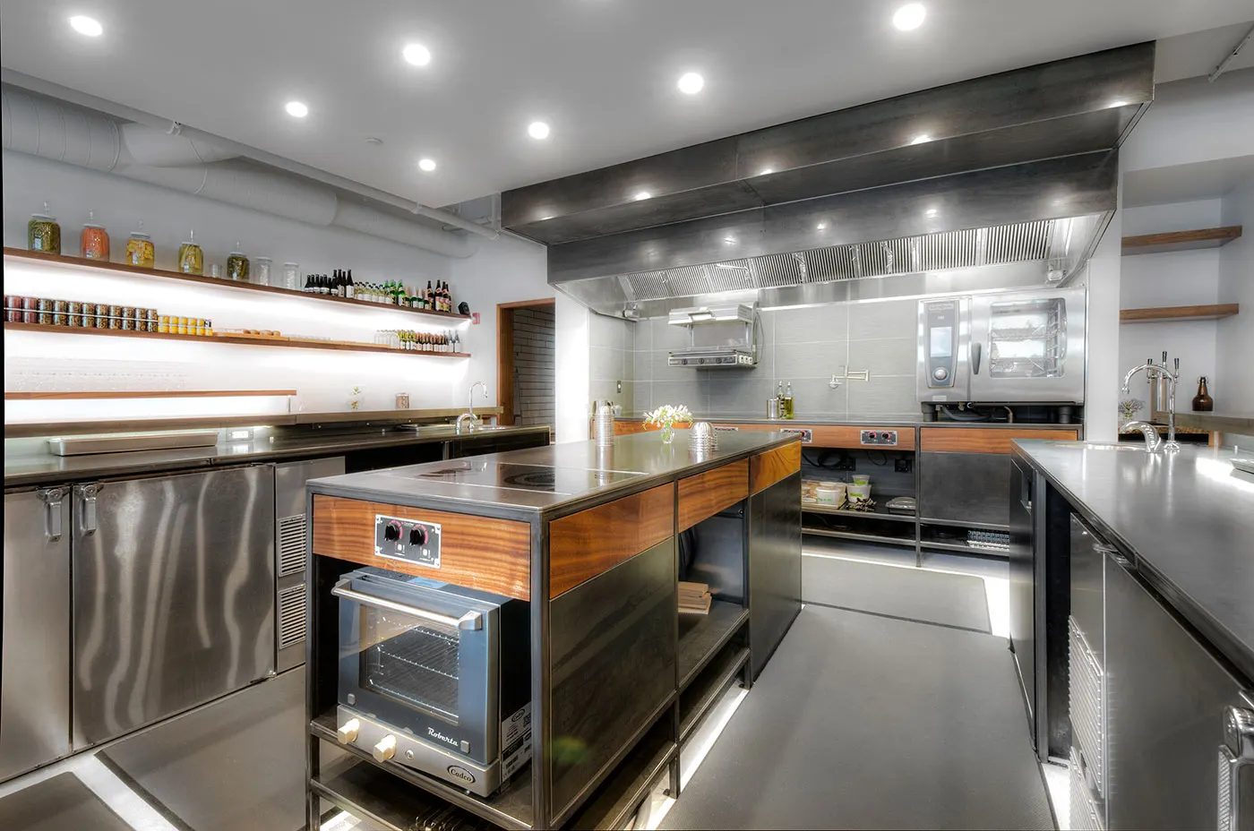 Stainless steel and timber stations under a blackened steel hood, with a small oven set into the island.