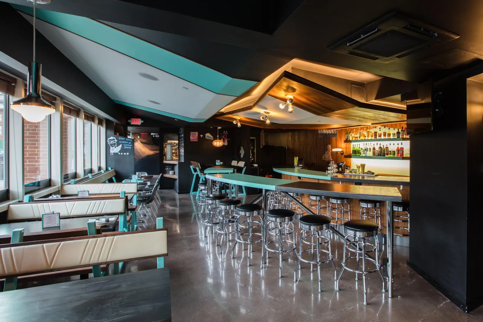 The bar and its stools seen past the booths, under the teal ceiling.
