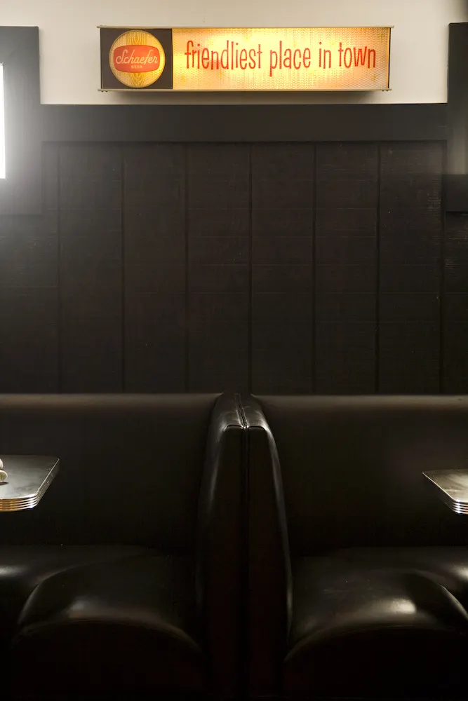 A dark leather booth under a lit sign reading friendliest place in town.