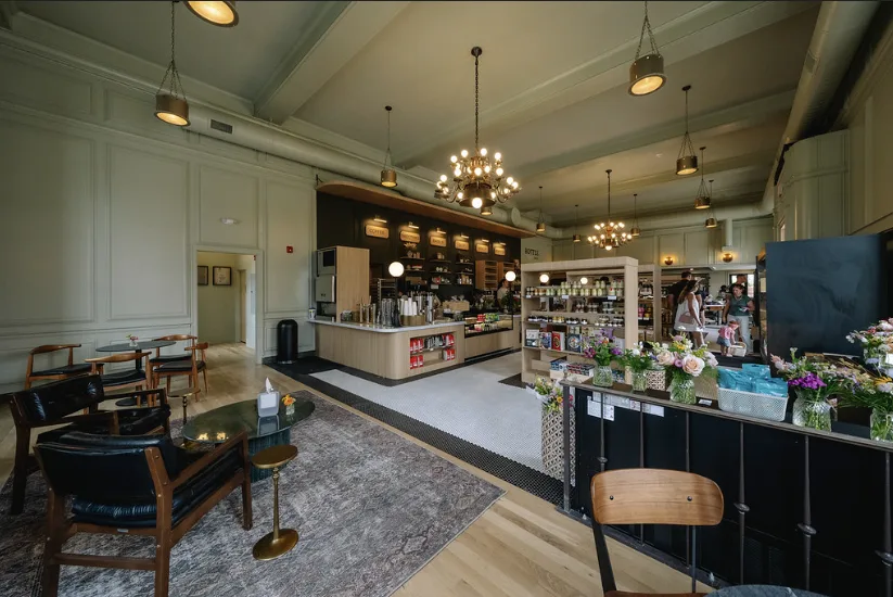 Leather chairs and small tables by the windows, with the counters and a chandelier beyond.
