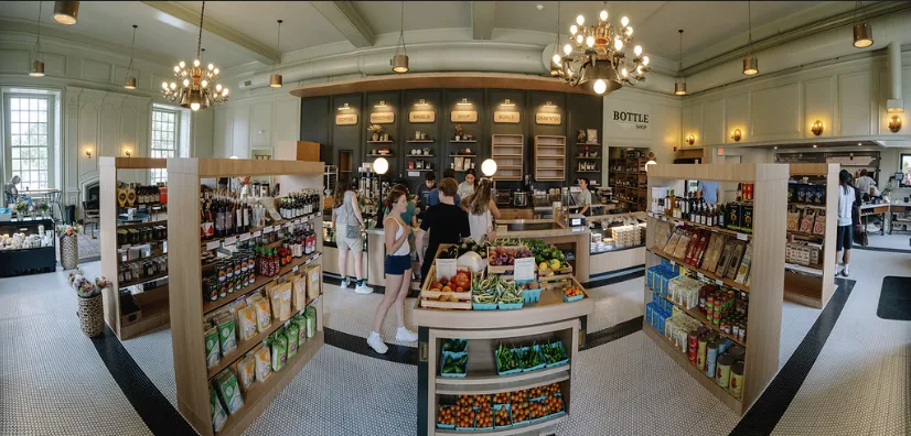 The market floor in one wide view: timber shelving islands and produce under a panelled ceiling and chandeliers.