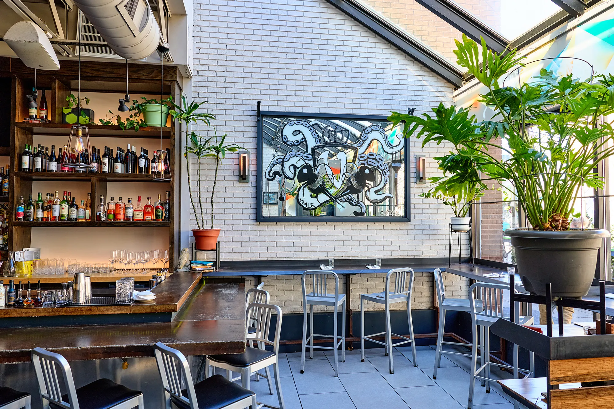 The bar and high tables under the glass roof, with plants and a framed artwork.