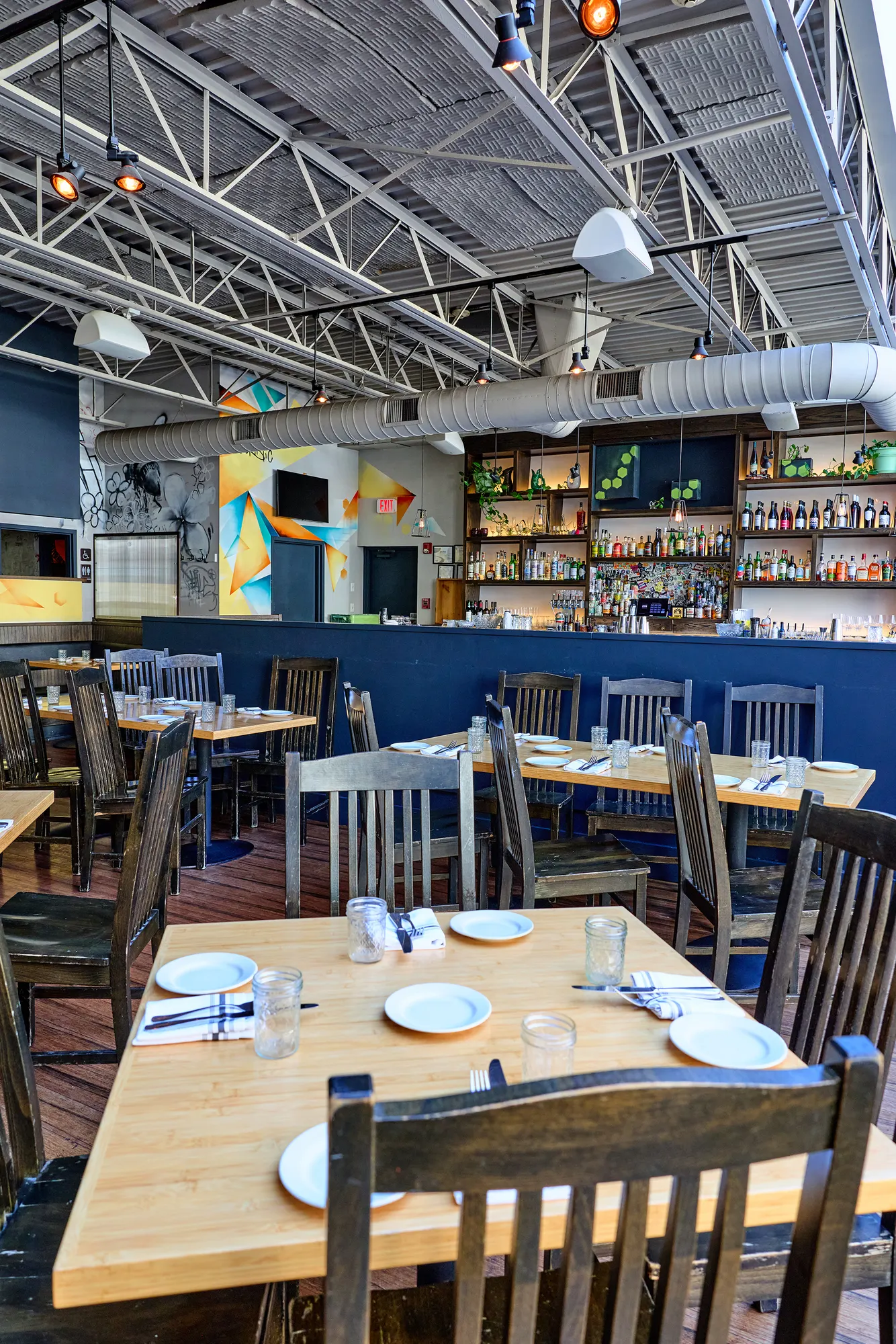 Tables set with plates under the steel roof trusses, with the bar beyond.