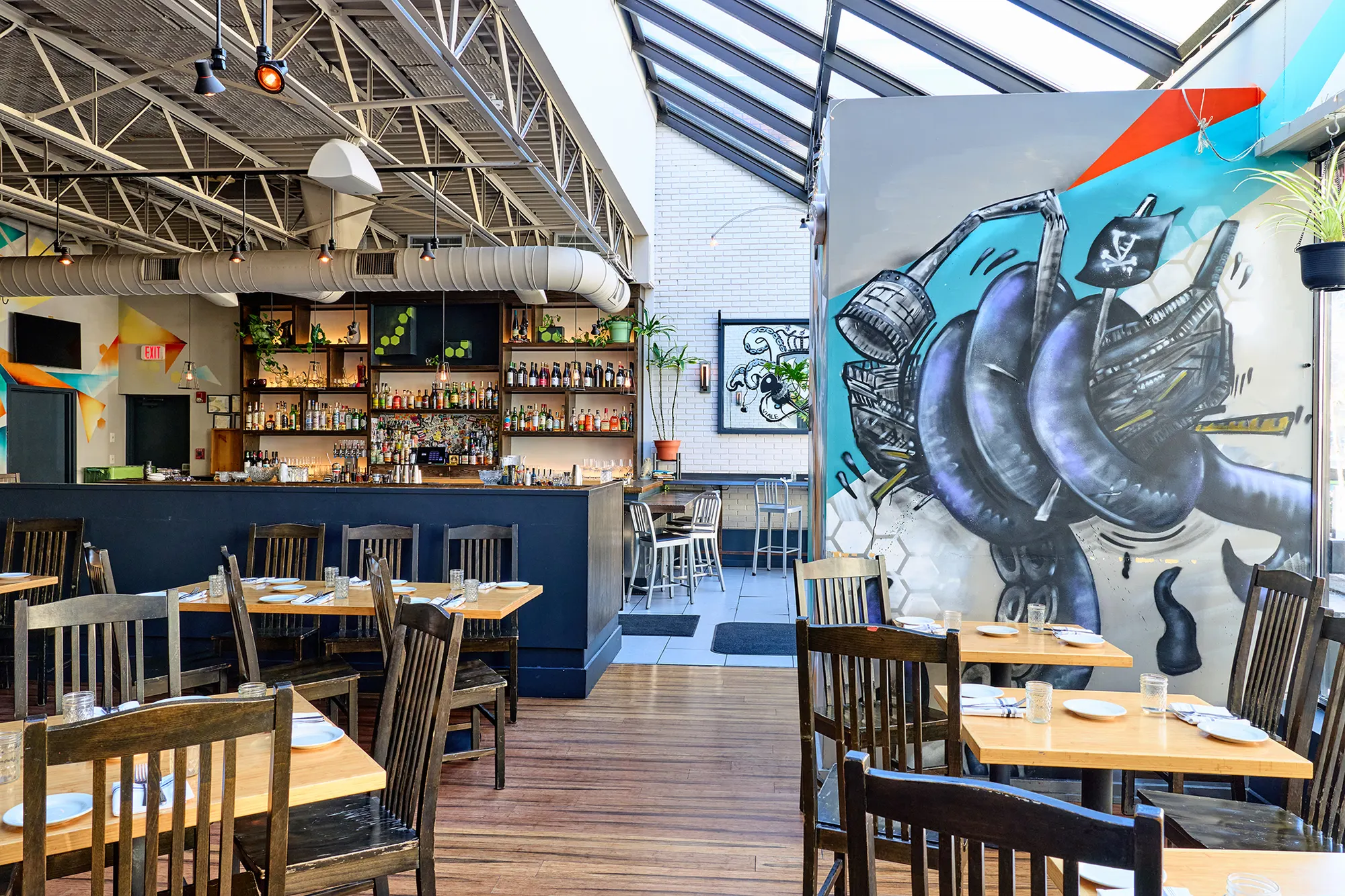 Tables in front of a painted mural of a helmeted figure, with the bar beyond.