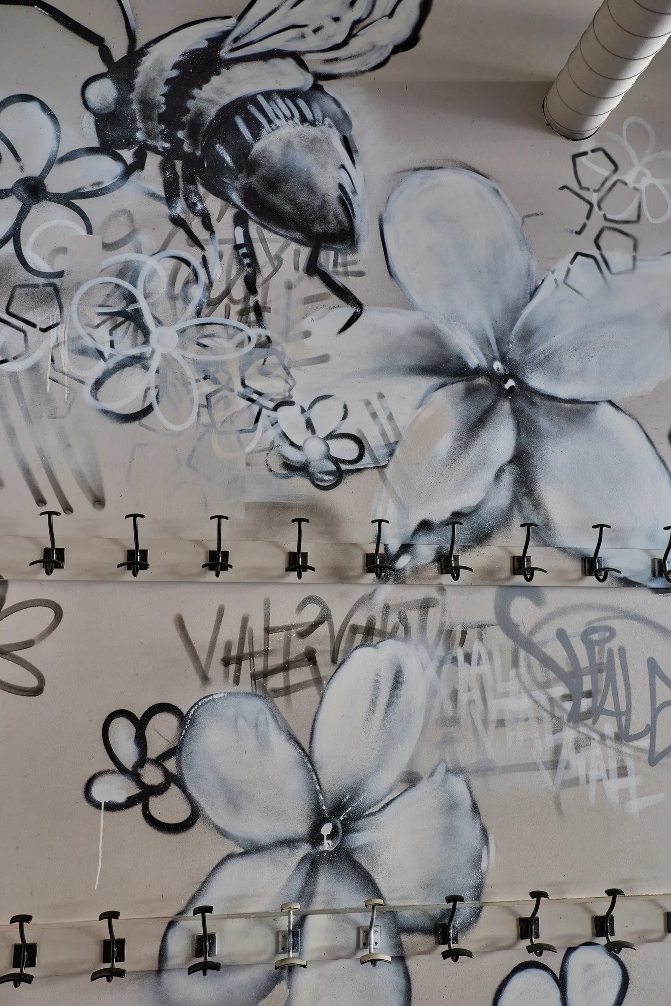 A painted bee among flowers above a row of coat hooks.