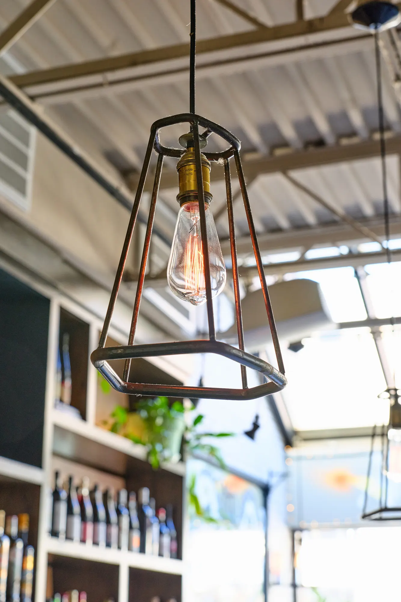 A caged pendant lamp hanging in front of wine shelves.