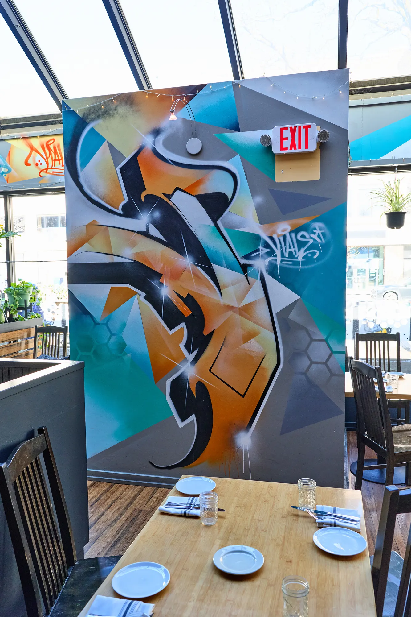 A table in front of a bold graffiti mural and an exit sign.