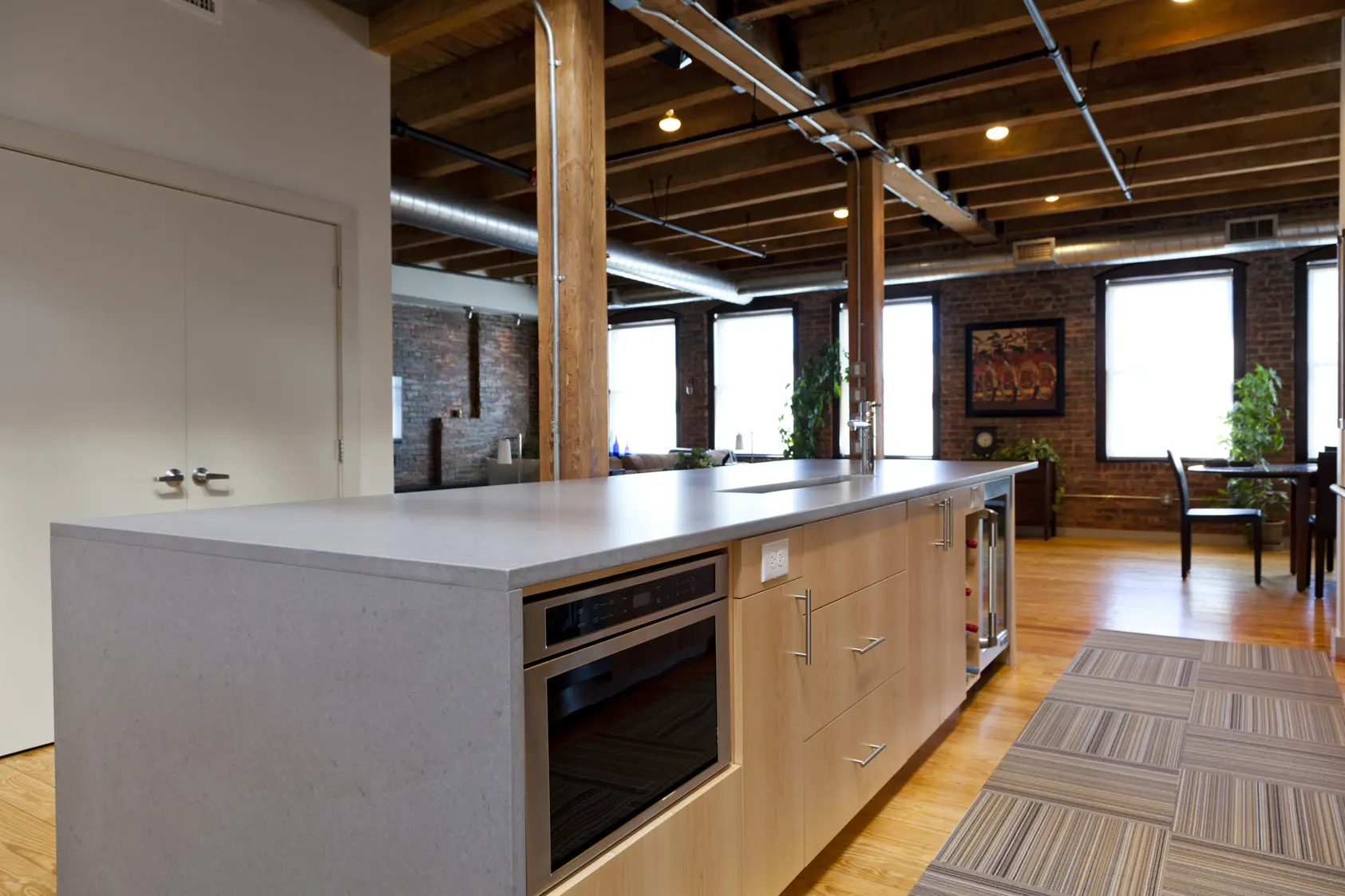 A concrete island with a built-in oven, the living room and brick walls beyond.