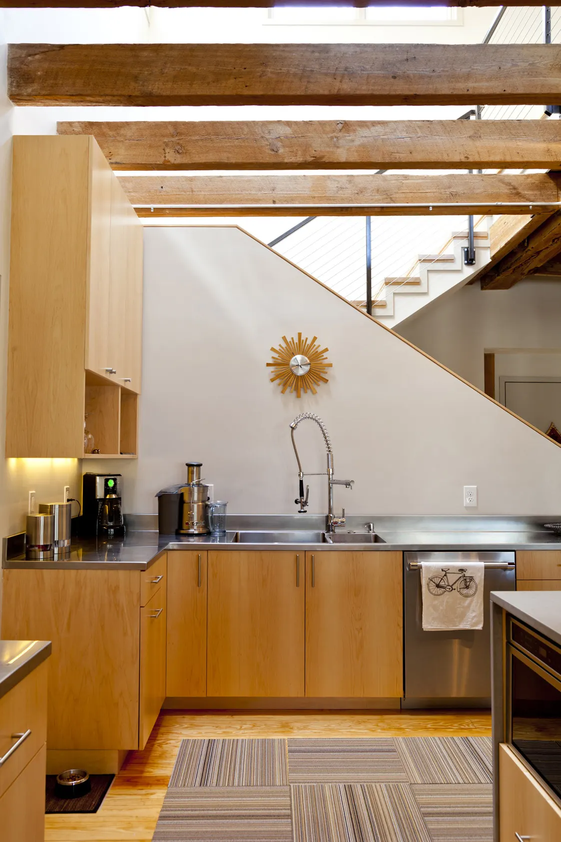 Maple cabinets and a steel sink tucked under the stair, with a sunburst clock on the wall.
