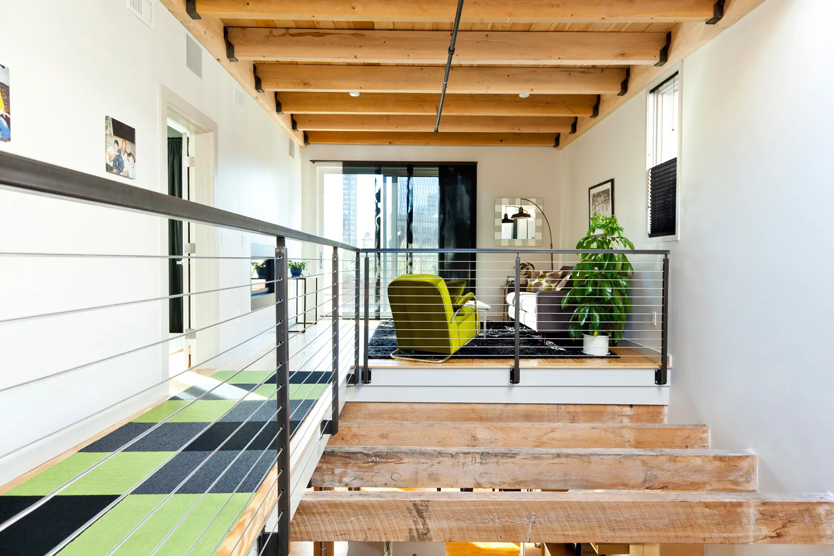 Timber treads rising to an upper floor with a green chair, a green and black tiled floor and a timber ceiling.