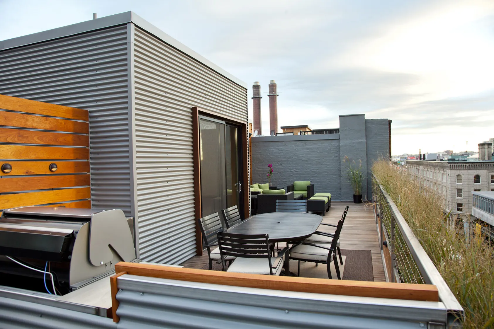 The dining table and grill beside the corrugated penthouse, with grasses along the rail.