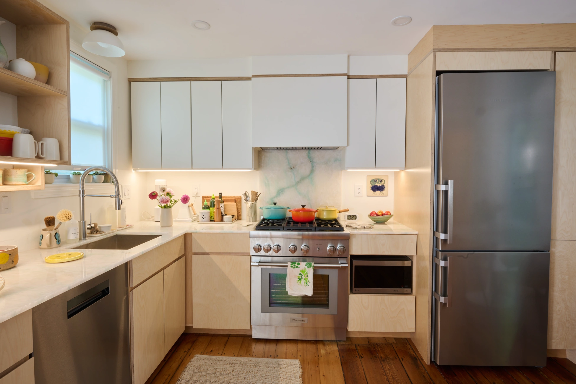 Birch base cabinets and white upper cabinets around a steel range and a tall steel refrigerator, with a marbled backsplash.