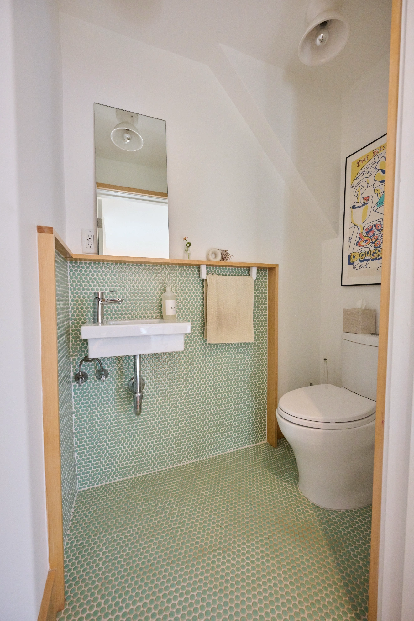 A small wall-hung basin and toilet in a room tiled in pale green penny tile, edged in birch.