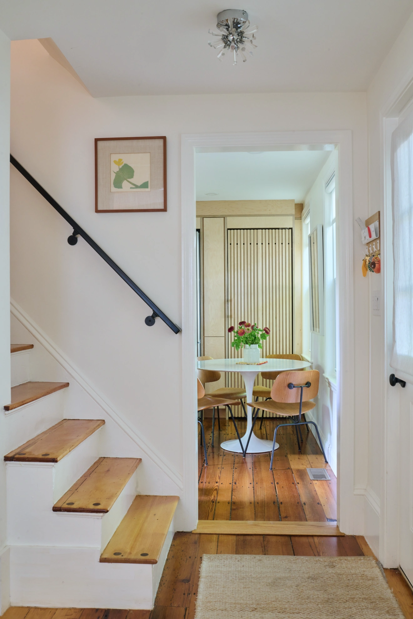A stair with birch treads and a black handrail, looking through a doorway to the dining table.