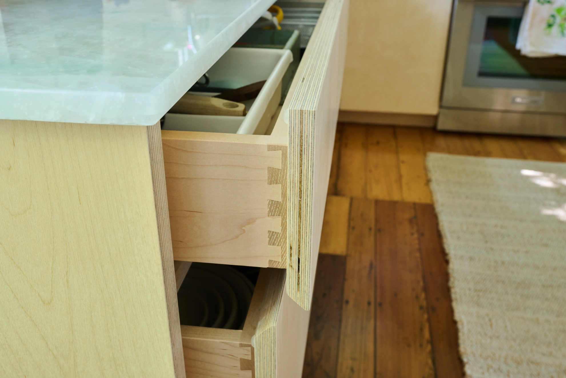 Birch drawers with dovetailed corners pulled open under a marble counter.